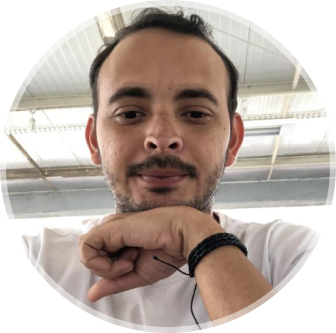 Foto de Mayk Brito sorrindo, usando óculos e camisa preta, barba e fundo amarelo.